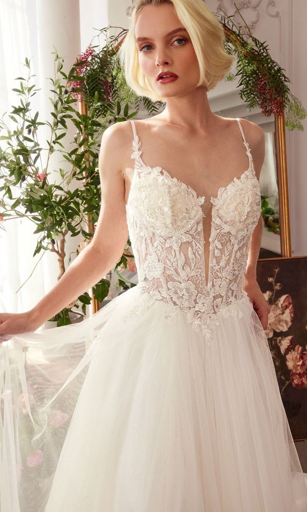 A woman in the Andrea and Leo WL029 long wedding dress with a sleeveless lace corset bodice stands indoors near greenery and a mirror.